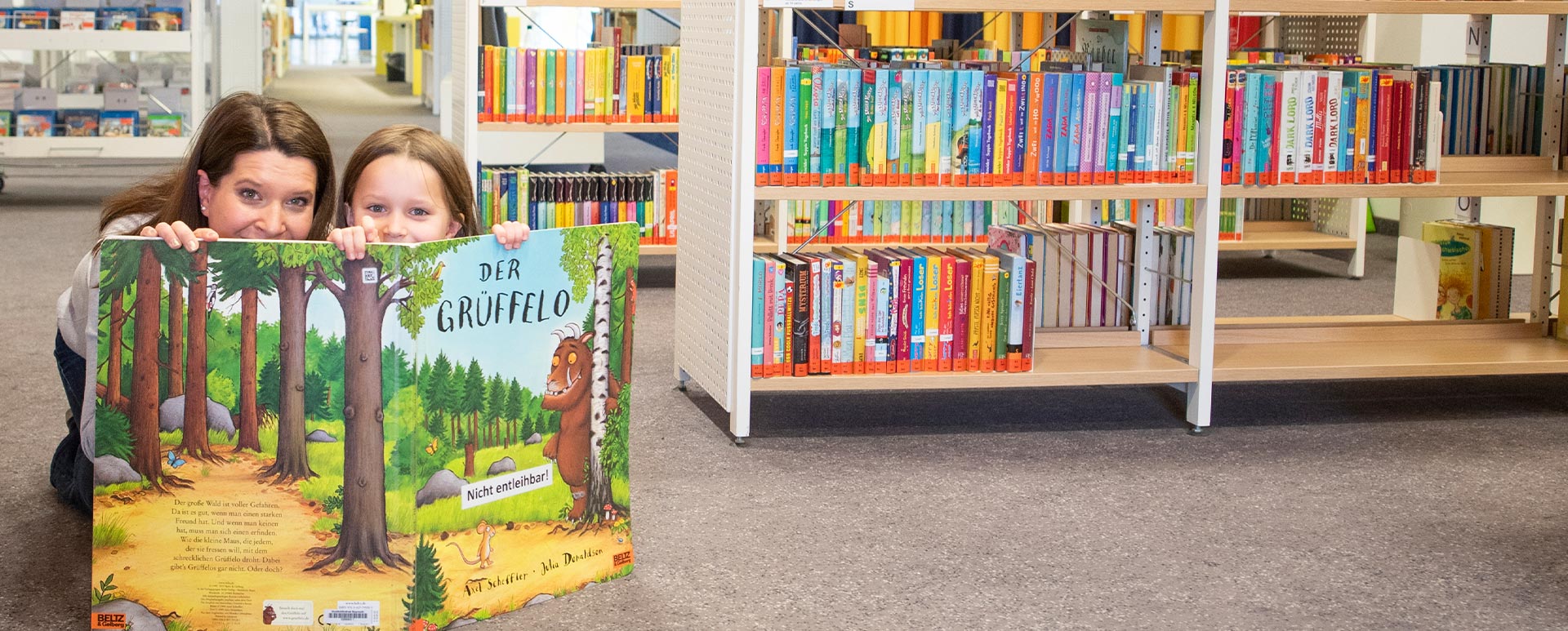 RW21 Stadtbibliothek – Frau versteckt sich mit Kind hinter Buch
