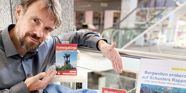 Mann mit Bart zeigt einen Wanderführer