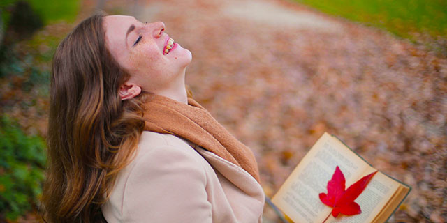 Frau liest ein Buch, in dem ein Herbstlaub liegt und lacht