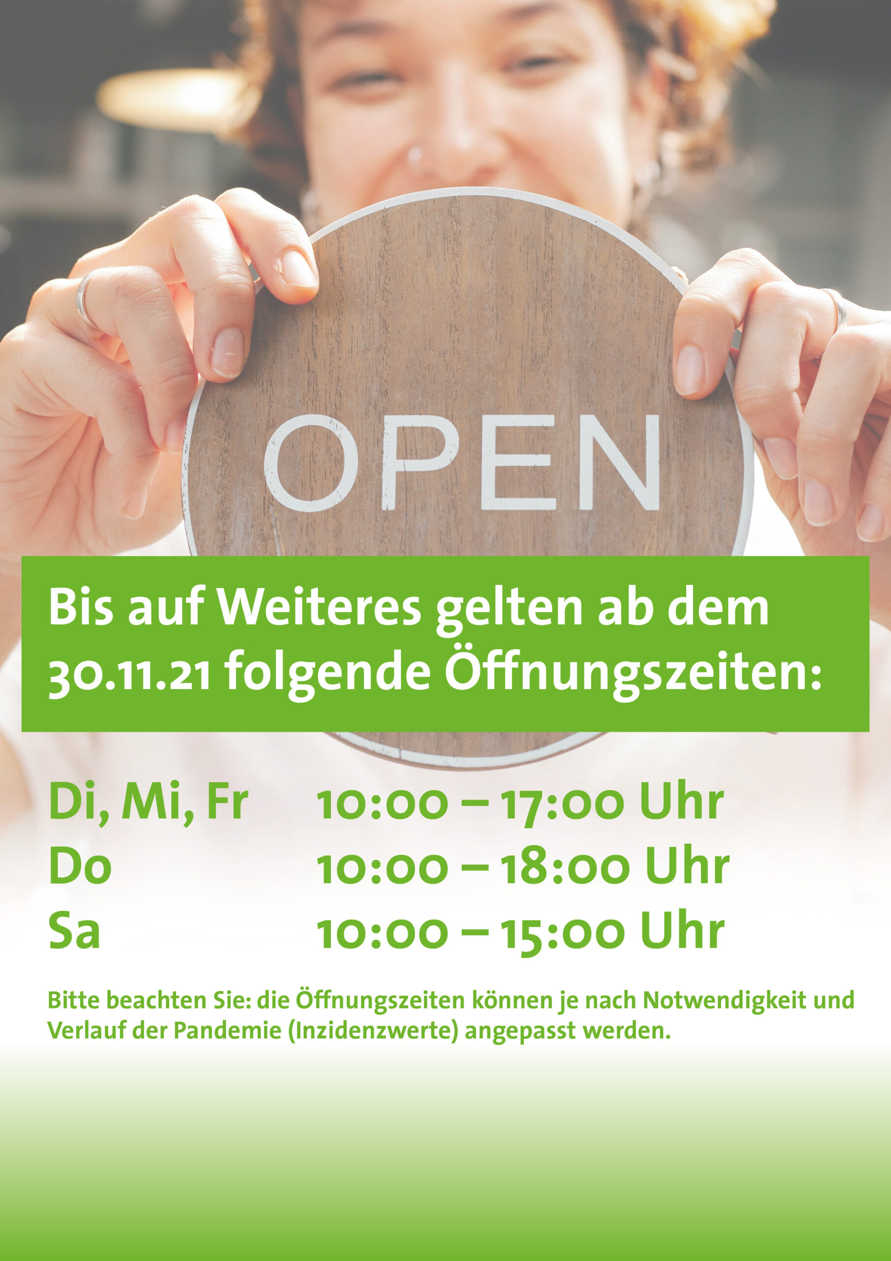 Eine junge Frau hält ein geöffnet Schild. Davor stehen die neuen Öffnungszeiten als Text.