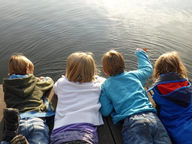 Kinder liegen auf einen Steg und schauen aufs Wasser