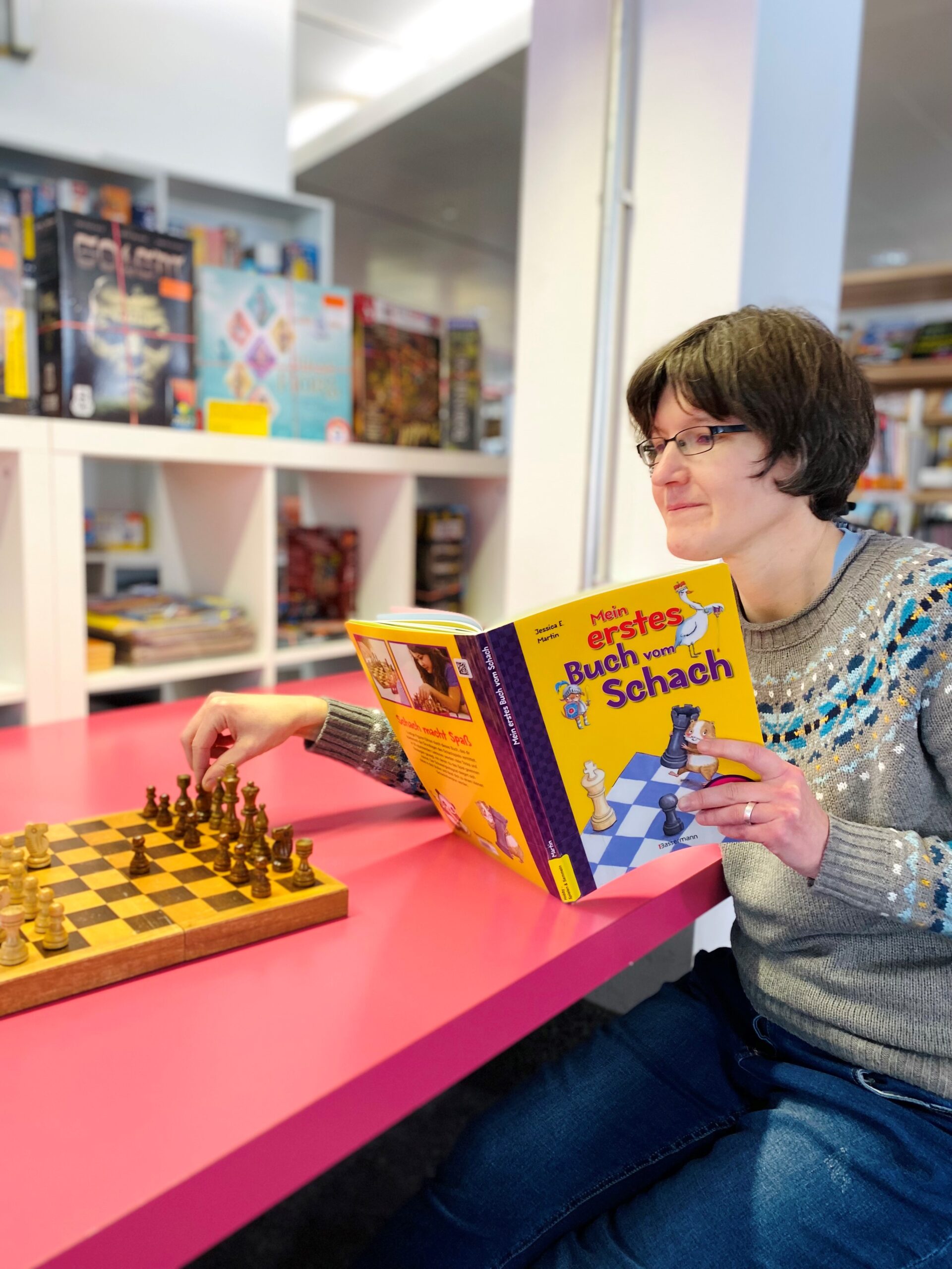 Frau spielt Schach und liest dabei ein Fachbuch für Spielanleitungen.