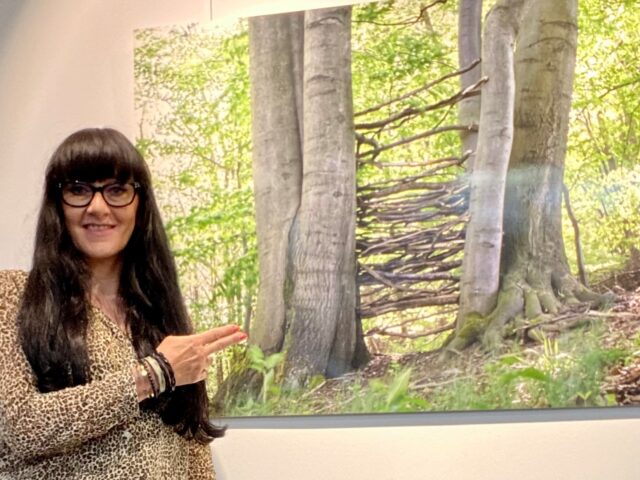 Frau mit Brille vor einer Fotografie mit Baum und Ästen