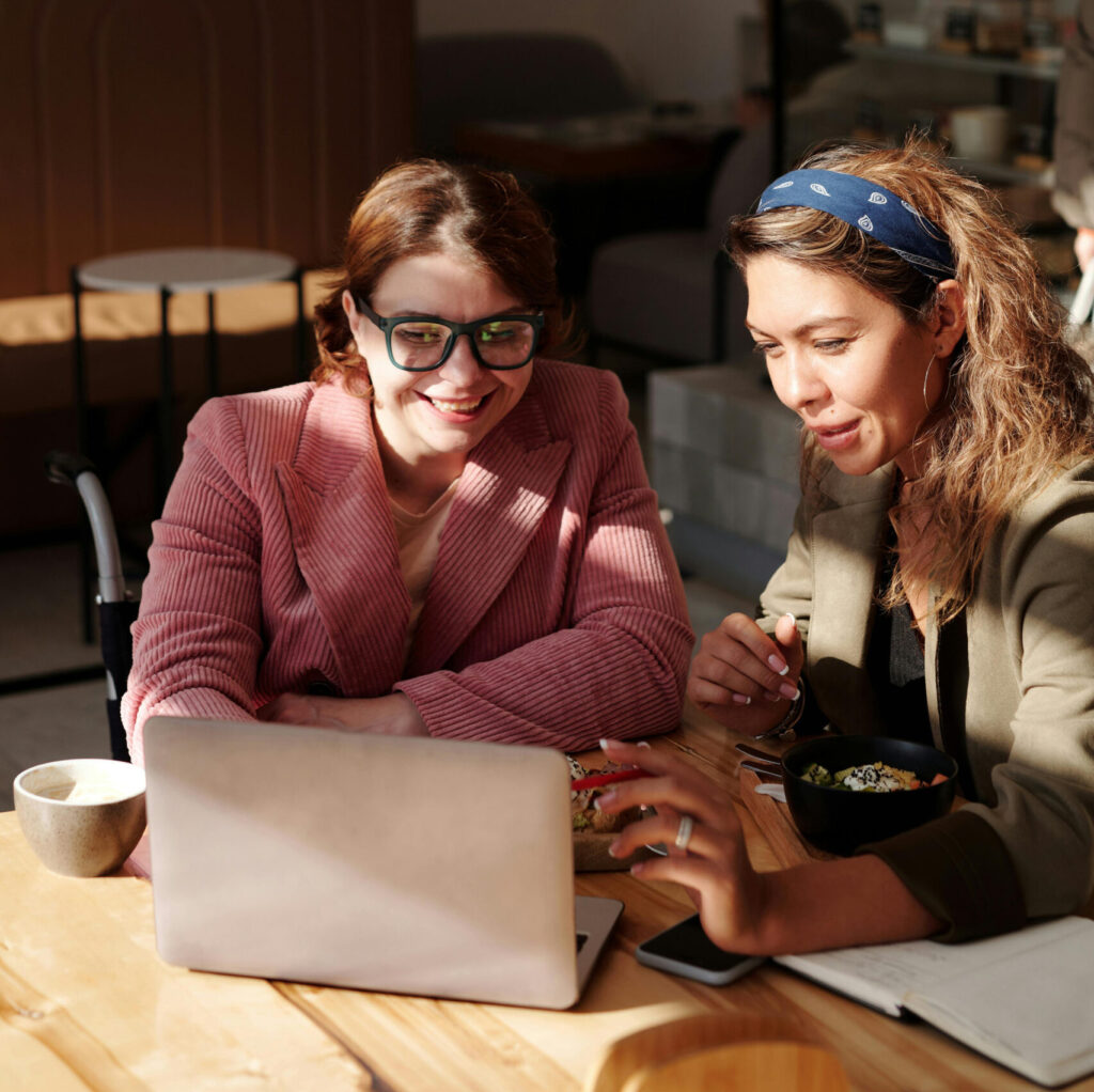 Zwei Frauen arbeiten an einem Laptop und lachen.