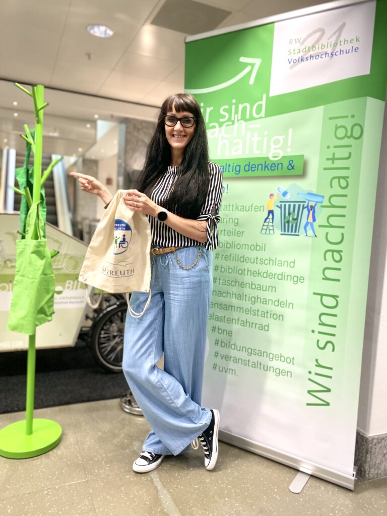 Frau mit Stofftasche steht vor grünem Garderobenständer.