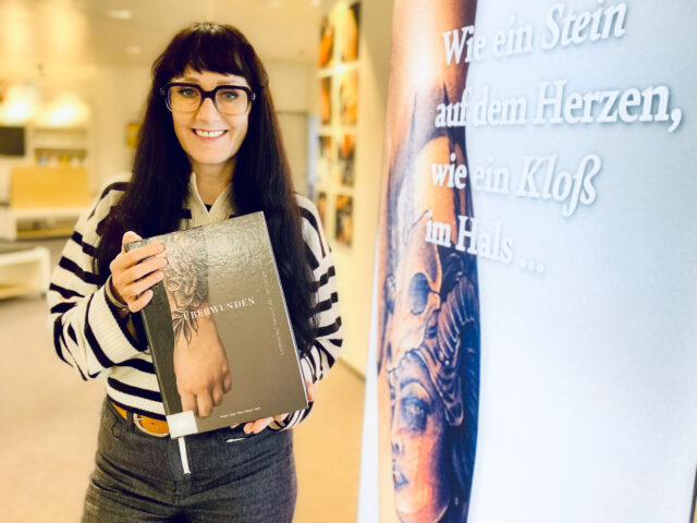 Frau mit Brille hält Buch in einer Ausstellung.