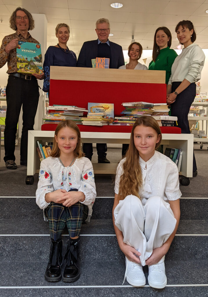 Eine Gruppe von Männern und Frauen und zwei Kindern freuen sich und halten Bücher in ukrainischer Sprache in die Kamera.