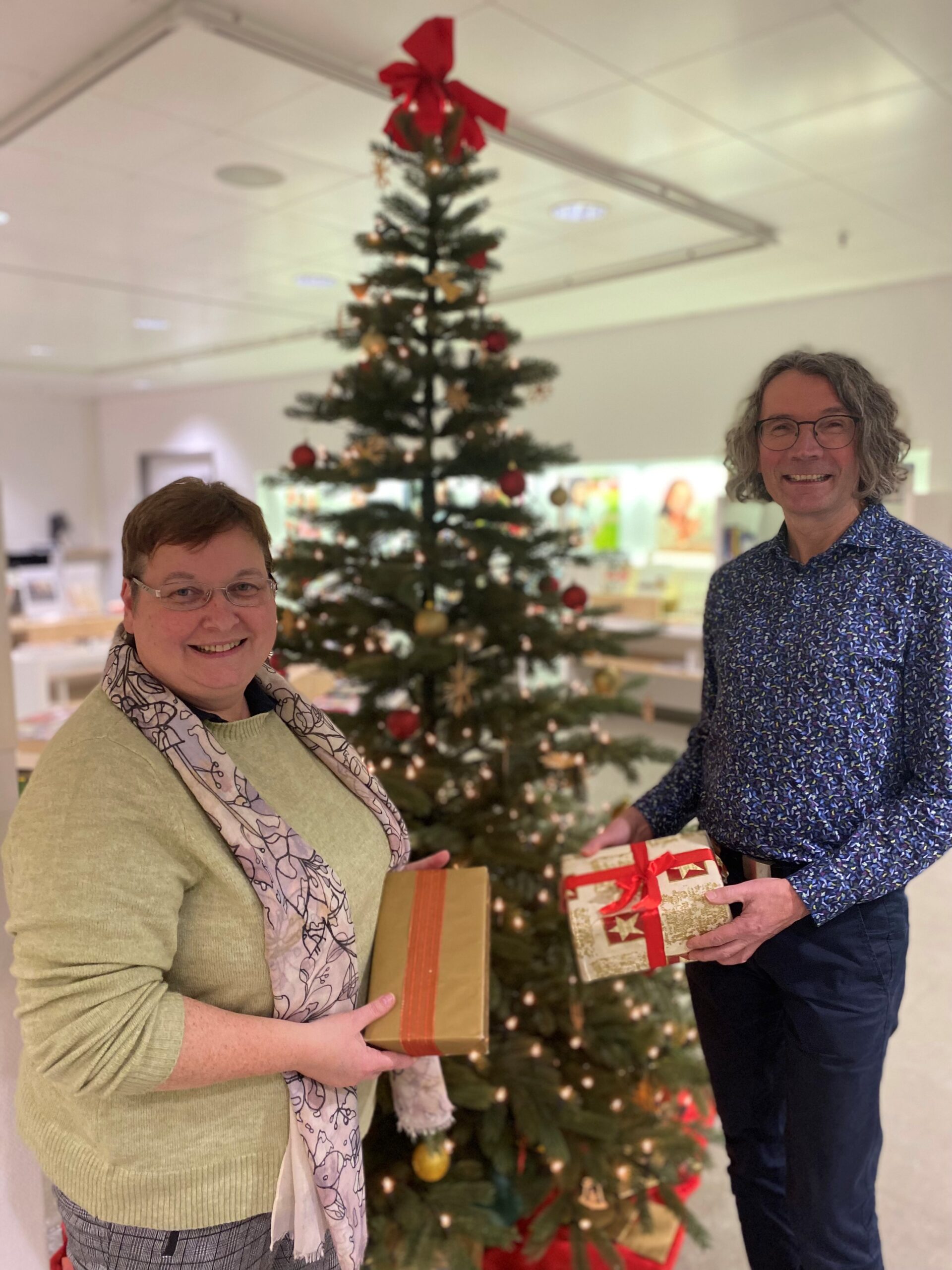 Ein Mann und eine Frau, stehen mit Geschenken in den Händen vor einem Weihnachtsbaum