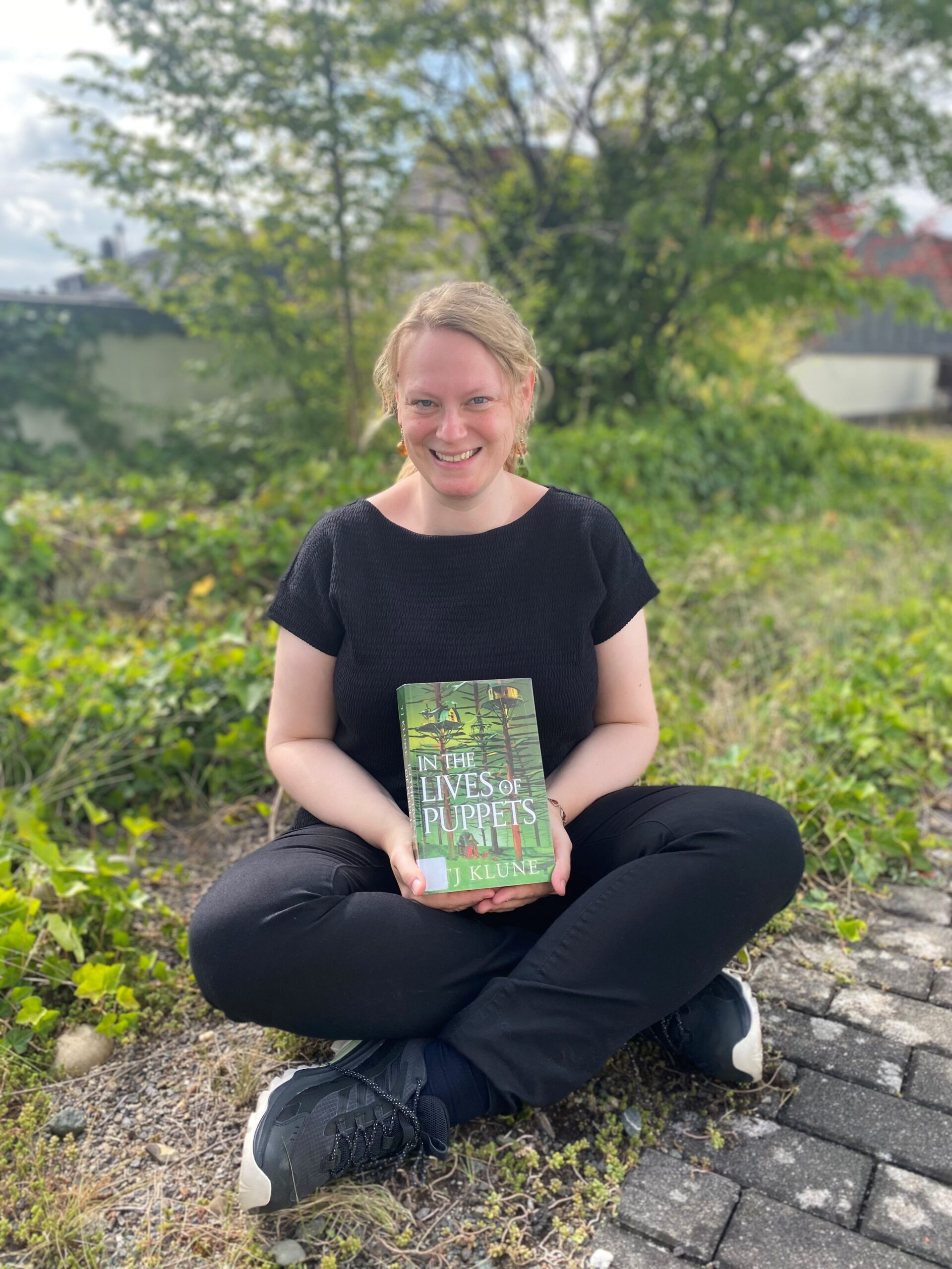 Frau sitzt mit einem Buch auf dem Boden im Freien.