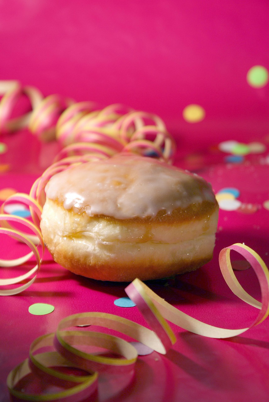 Krapfen und Konfetti mit Luftschlangen liegen auf pinkfarbigen Untergrund