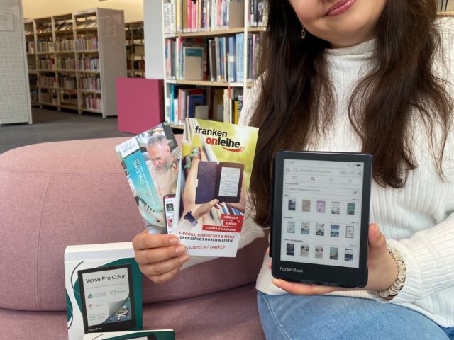 Eine junge Frau hält einen eBook-Reader sowie einige Flyer in der Hand.