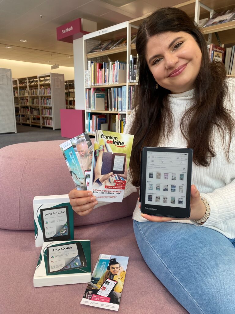 Eine junge Frau hält einen eBook-Reader sowie einige Flyer in der Hand.