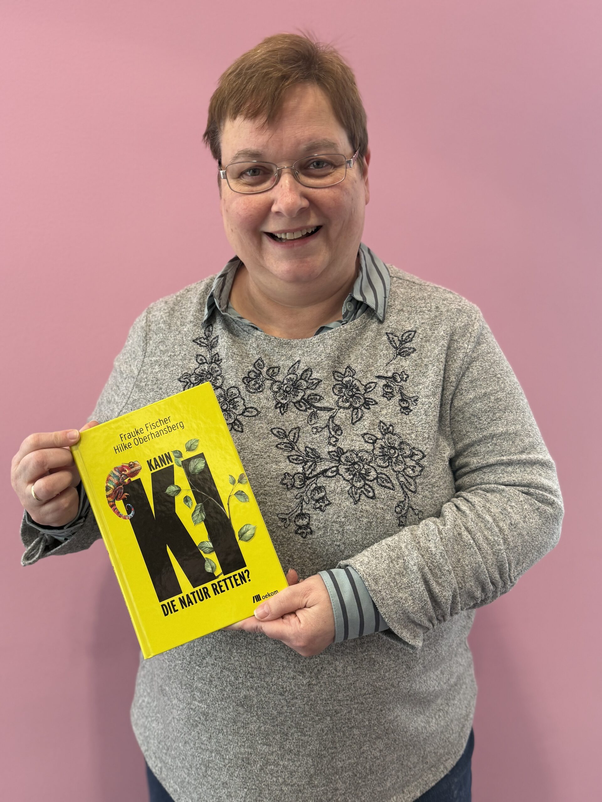 Eine Frau mit kurzen Haaren und Brille hält ein gelbes Buch in den Händen.