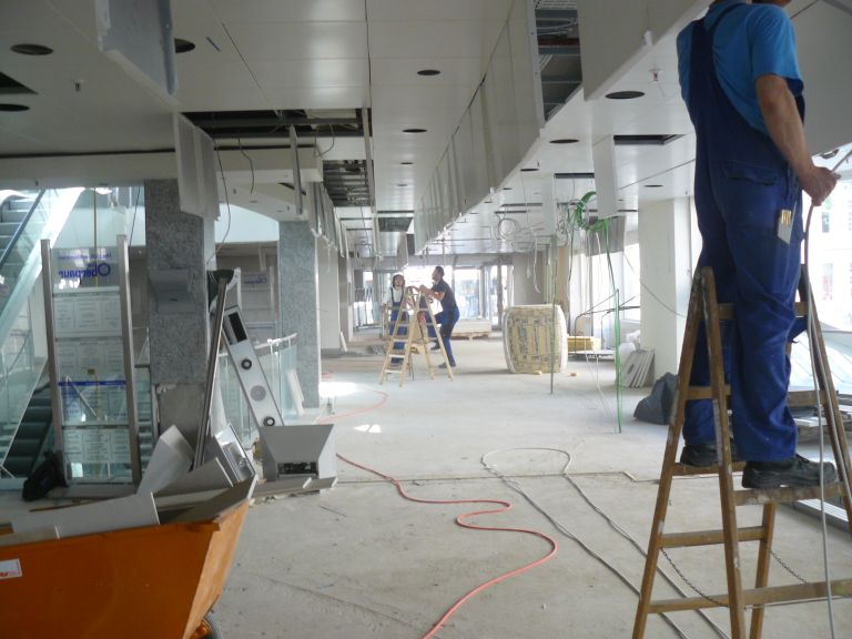 Eine Baustelle, ein Mann steht auf einer Leiter, es sind Kabel zu sehen, im Hintergrund ist ebenfalls eine Person mit einer Leiter.