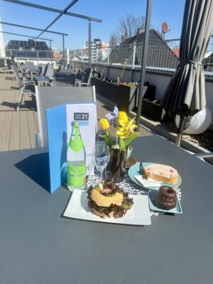 Ein Tisch auf einer Terrasse mit Speisen und Getränken sowie einer Blumenvase und einer Karte.