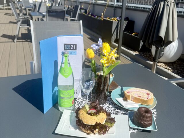 Ein Tisch auf einer Terrasse mit Speisen und Getränken sowie einer Blumenvase und einer Karte.